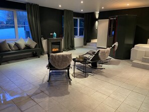 A modern living room with a fireplace, a sofa with cushions, a coffee table, and a large black cabinet. - Landhaus Foresta (Braunlage)