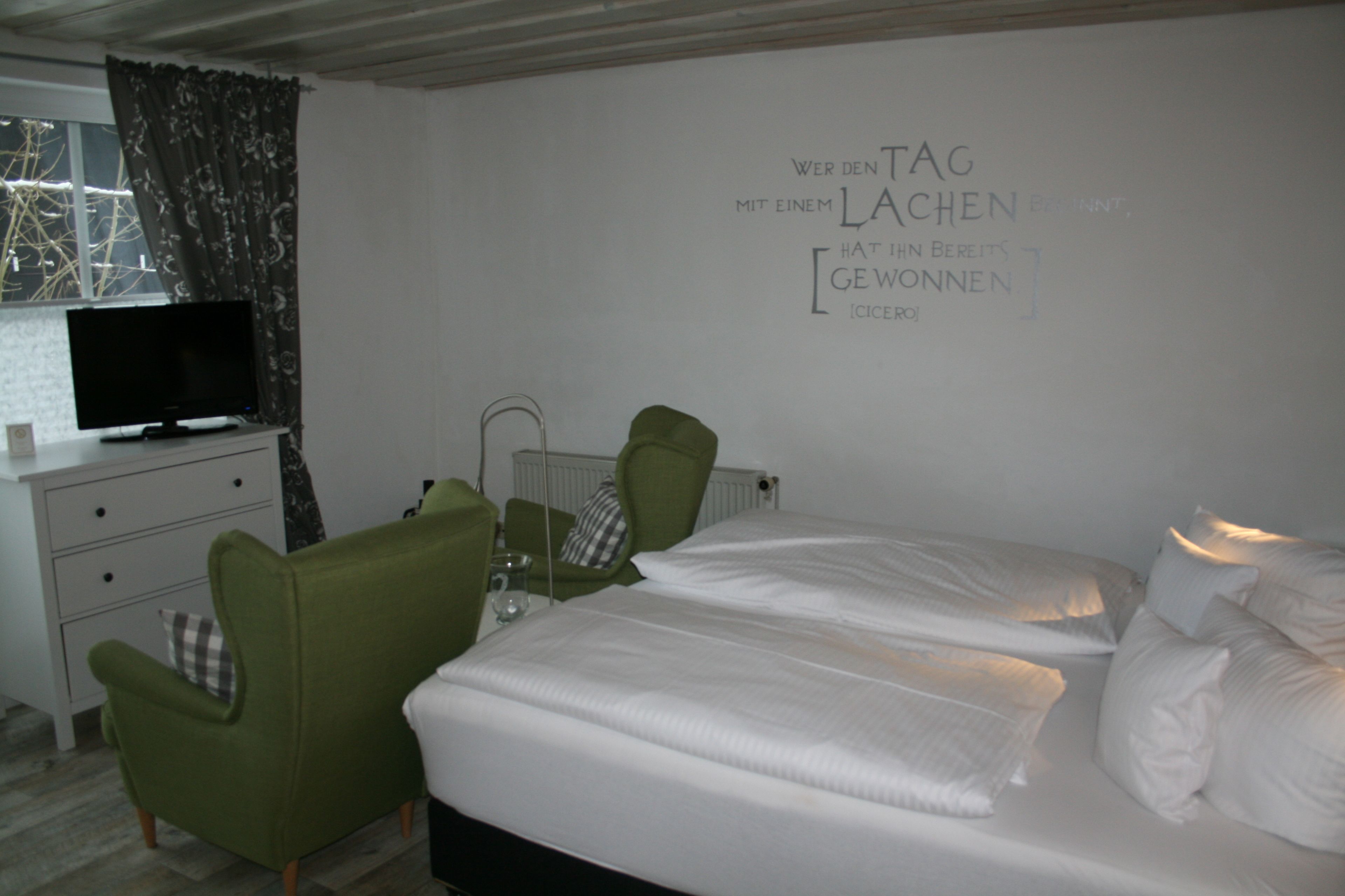 Una camera d'albergo con un letto, due poltrone, un televisore e una parete con una frase motivazionale.