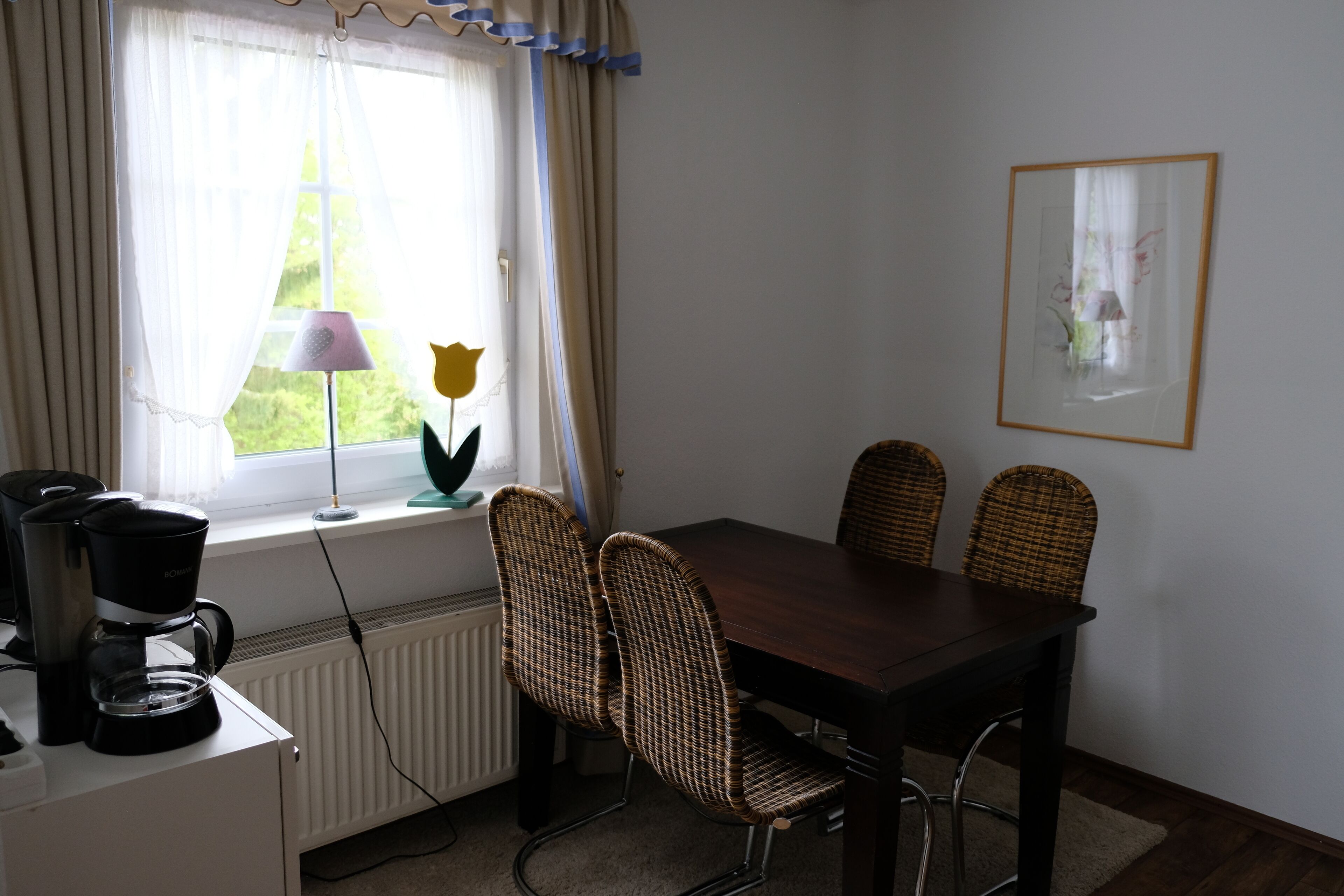 Un comedor con una mesa y sillas, una cafetera y un ventanal con cortinas.