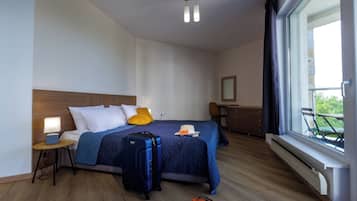 A hotel room with a bed, a suitcase, a nightstand, a lamp, a window with a view, and a chair.