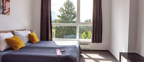 A bedroom with a bed, a window with curtains, a bench, and a painting on the wall.