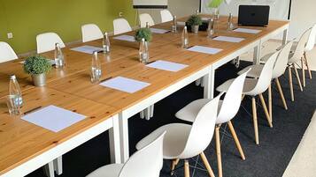 Un salón de conferencias con una larga mesa de madera, sillas blancas y una pantalla de proyector mostrando una presentación.