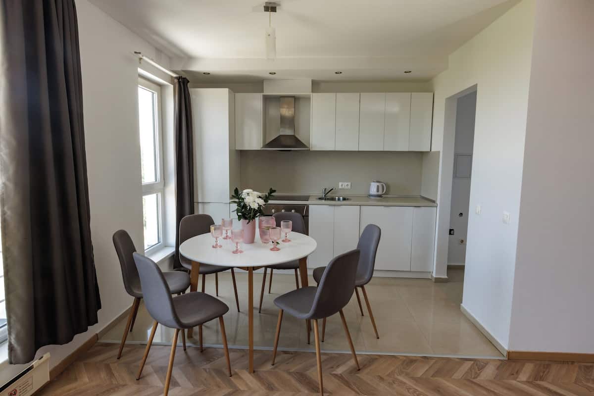 A modern kitchen with white cabinets, a central island, and a dining area with a round table and chairs.