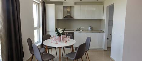 Una cocina moderna con armarios blancos, una isla central y un comedor con mesa redonda y sillas.