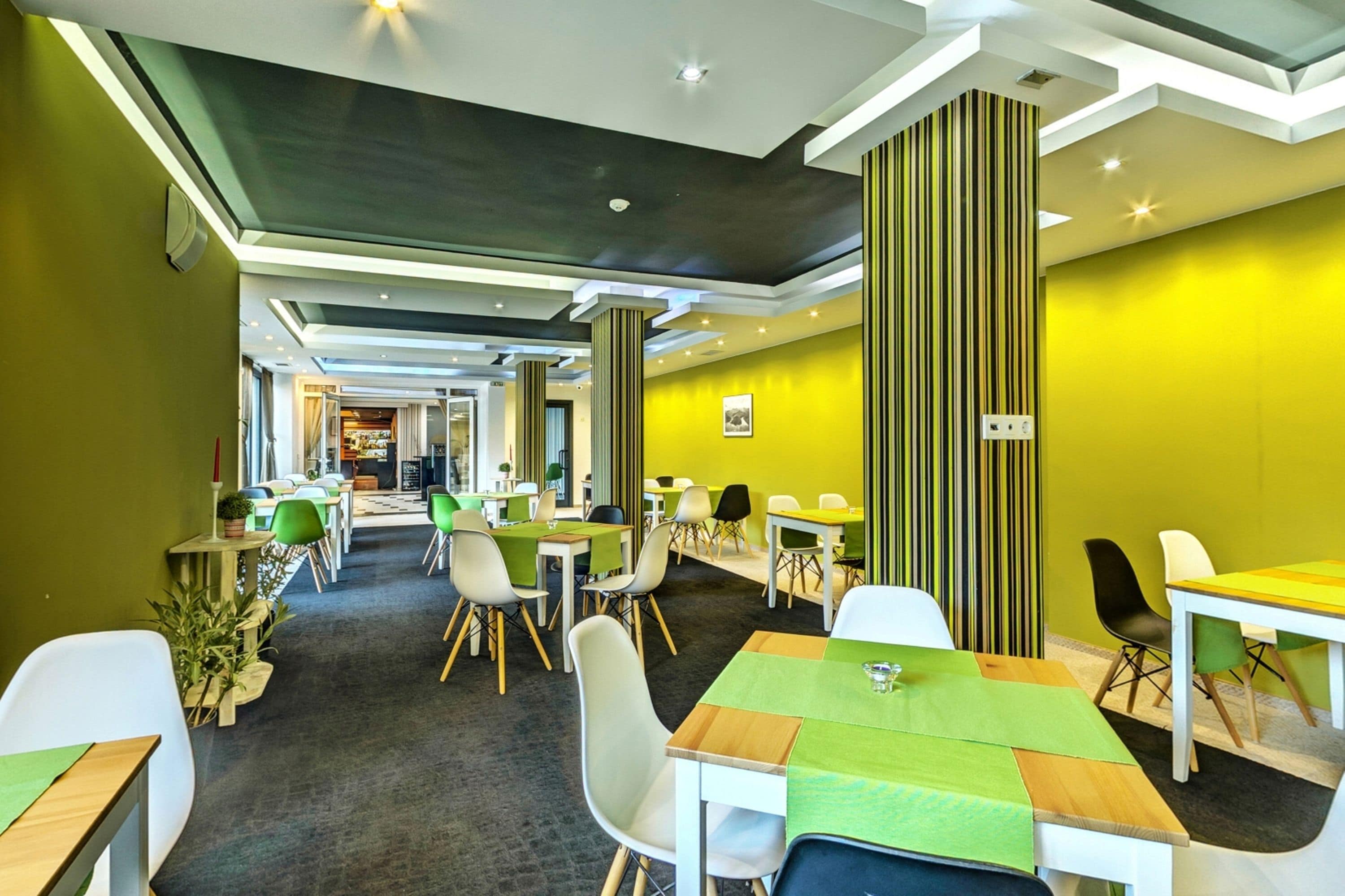 A modern dining area with tables and chairs, a green carpet, and a striped column.