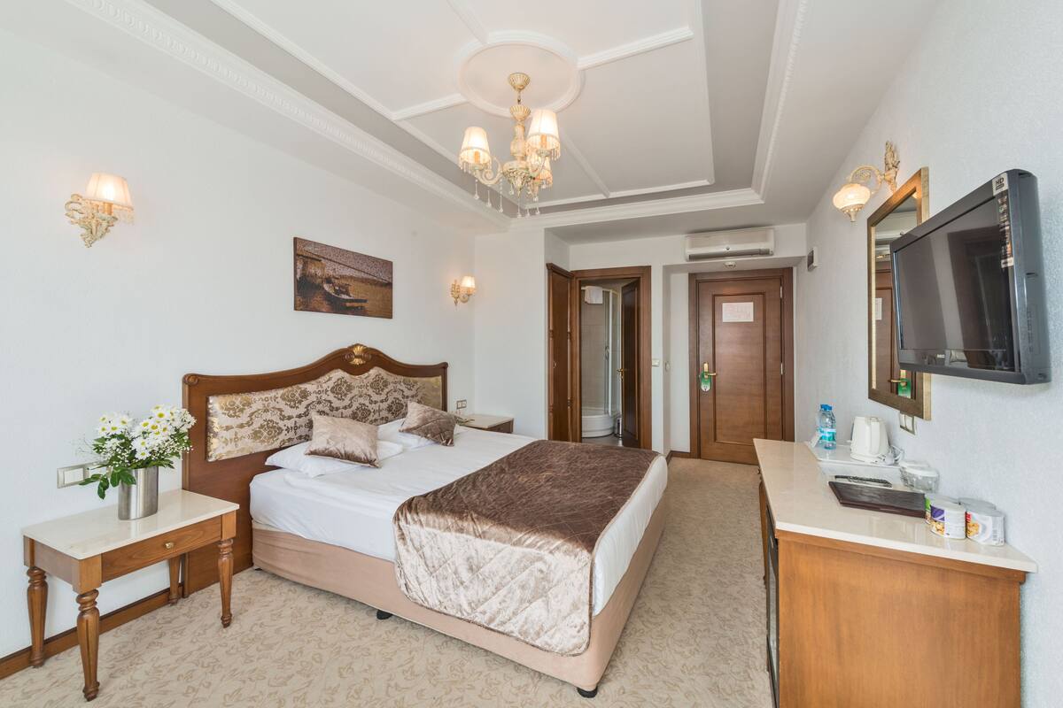 A hotel room with a bed, bedside tables, a desk, a television, and a bathroom door.