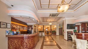 A hotel lobby with a reception desk, chairs, a chandelier, and a television.