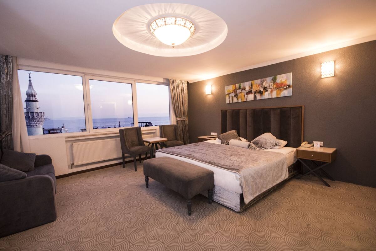 A hotel room with a large bed, a desk, a chair, and a view of a tower through the window.