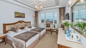 A hotel room with two beds, a sitting area with a view, a large mirror, and a chandelier.
