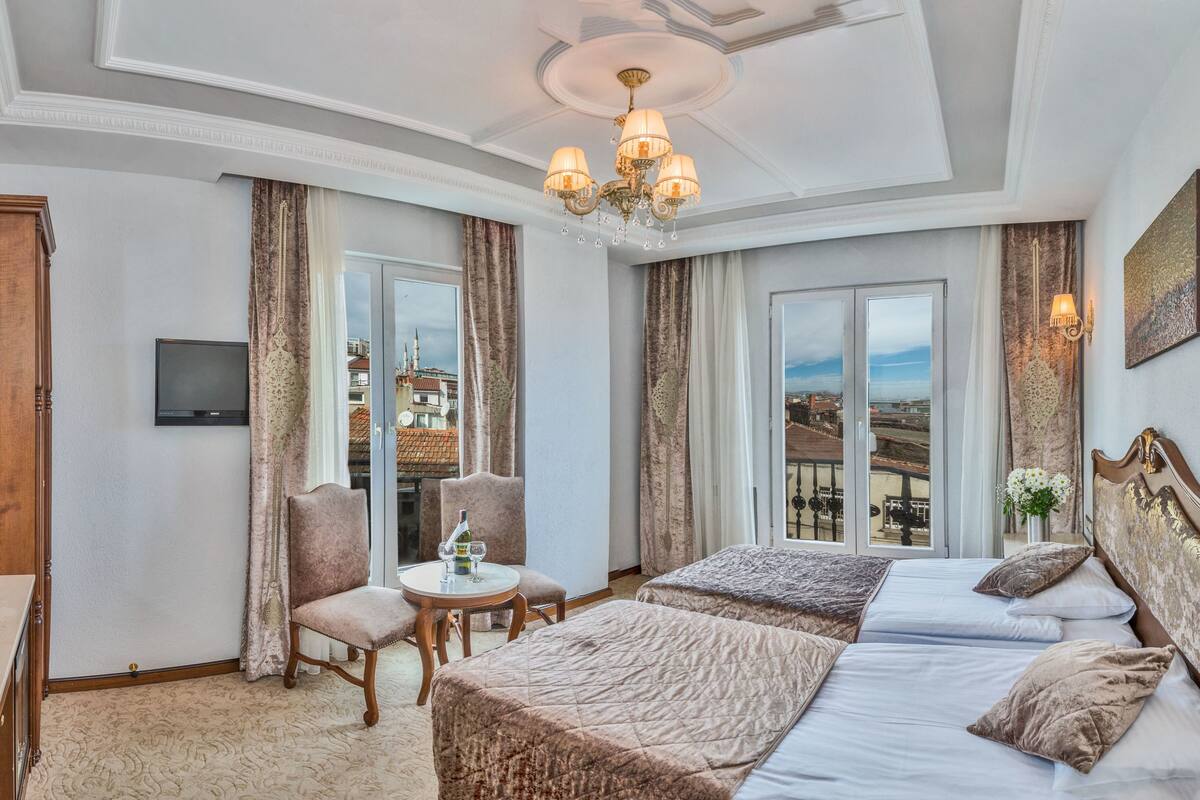 A hotel room with a large bed, a desk with a chair, a television, and a view of the city.