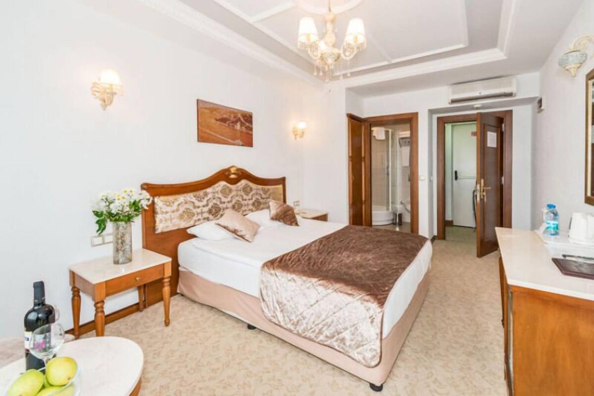 A hotel room with a bed, bedside table, a mirror, a small table with fruit, and a door leading to a bathroom.