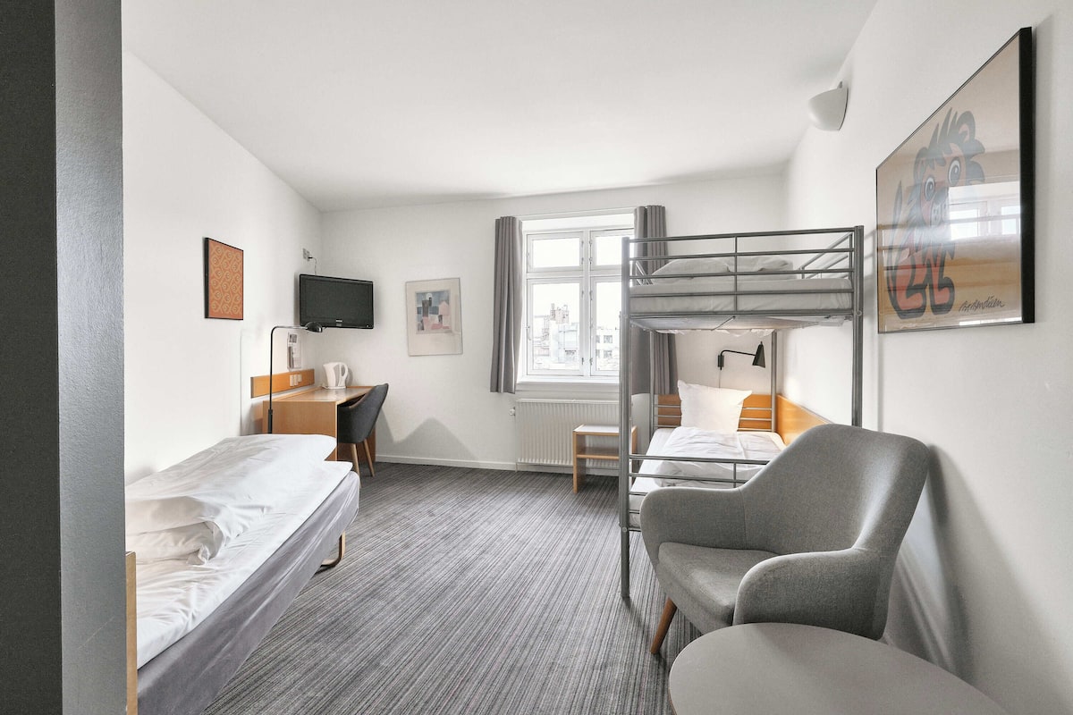 Ein Hotelzimmer mit Etagenbett, Schreibtisch, Stuhl, Fernseher und einem Fenster mit Vorhängen.