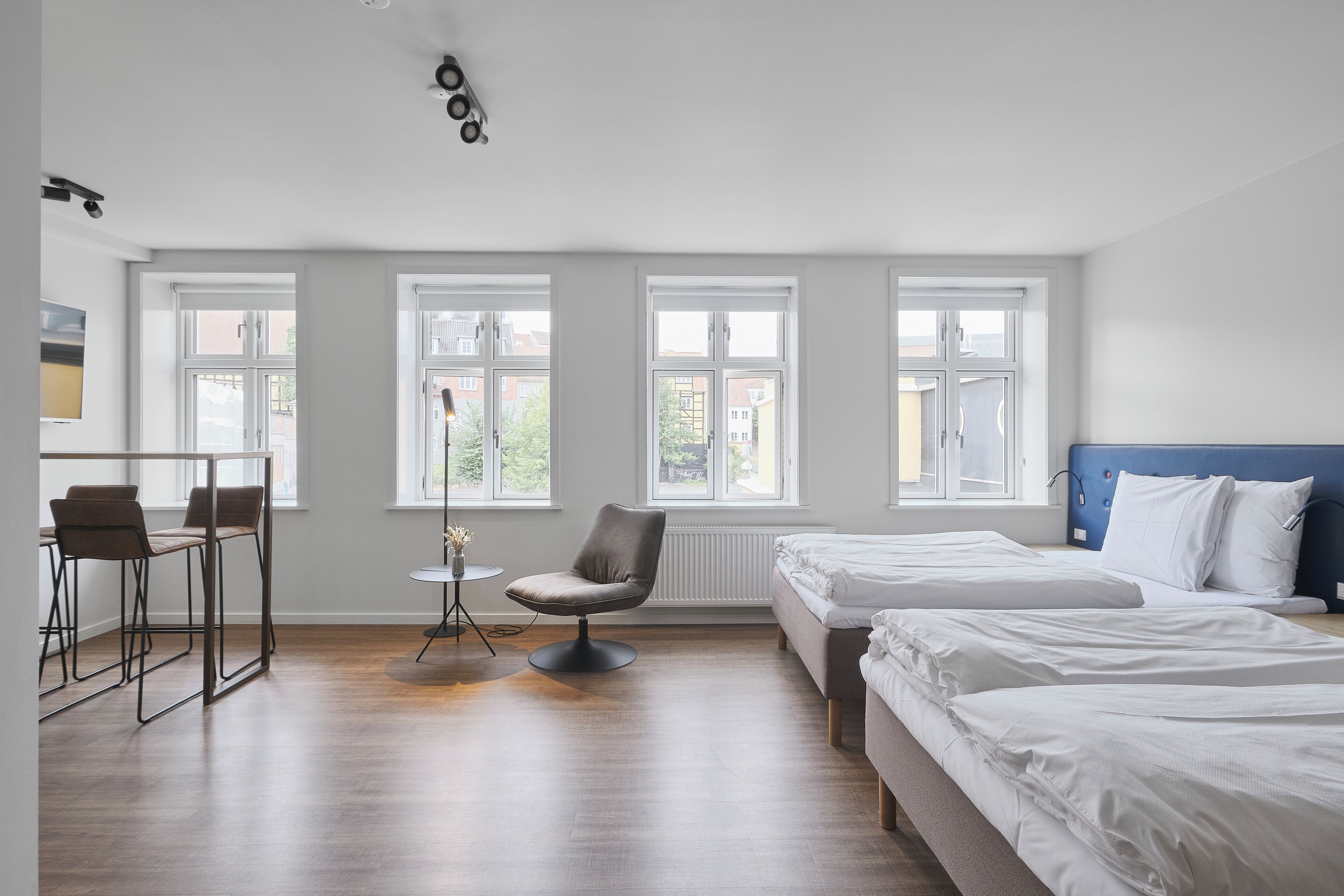 Habitación de hotel con dos camas, un comedor con sillas, una pequeña mesa y ventanas amplias.