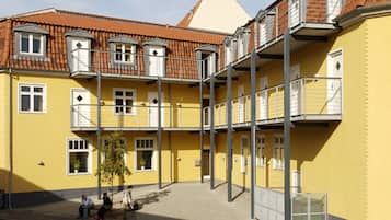 Un edificio amarillo de varios pisos con balcones, un patio central y un pequeño árbol.