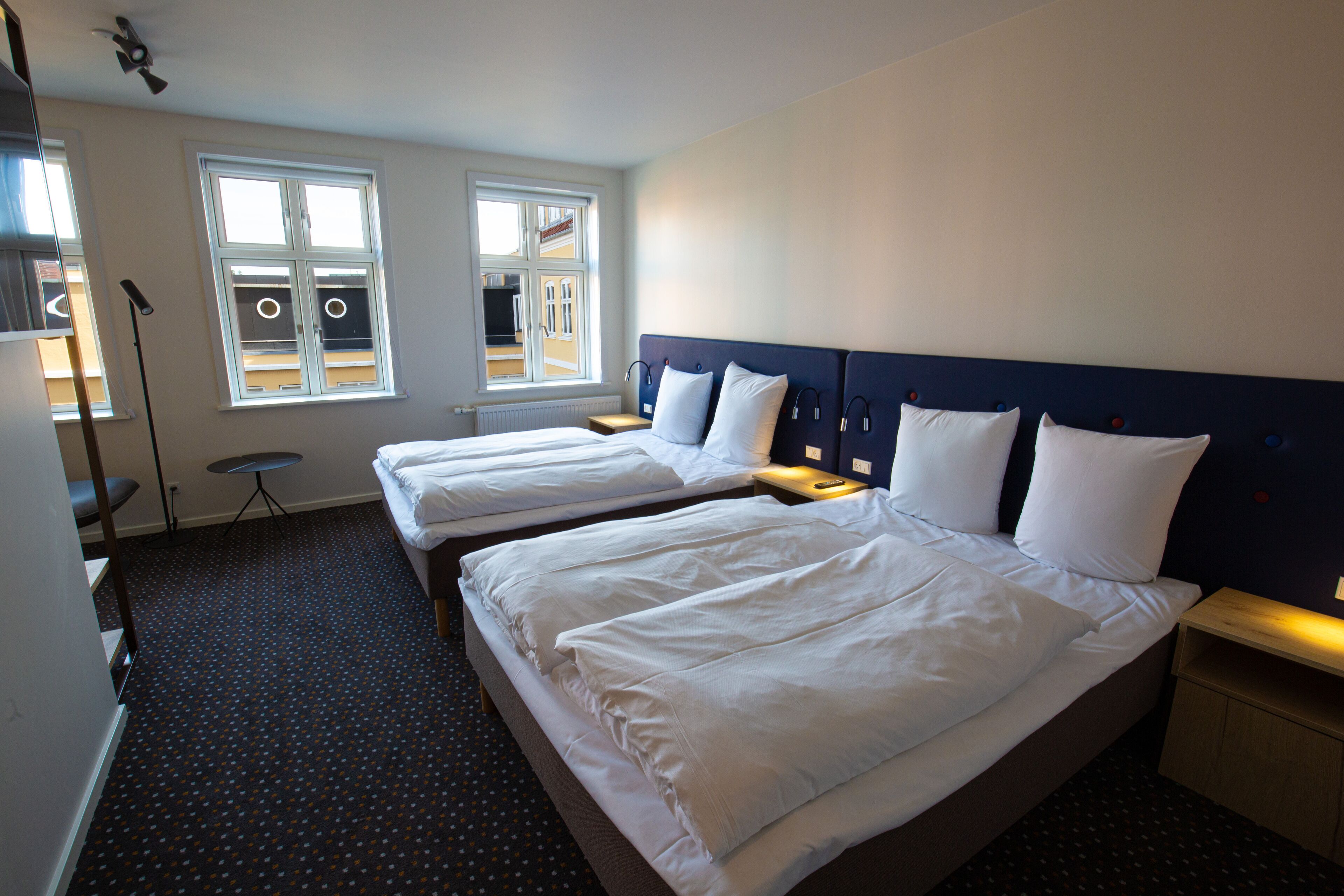 Ein Hotelzimmer mit zwei Betten, einem Fenster mit Jalousien, einem Schreibtisch und einer Lampe.