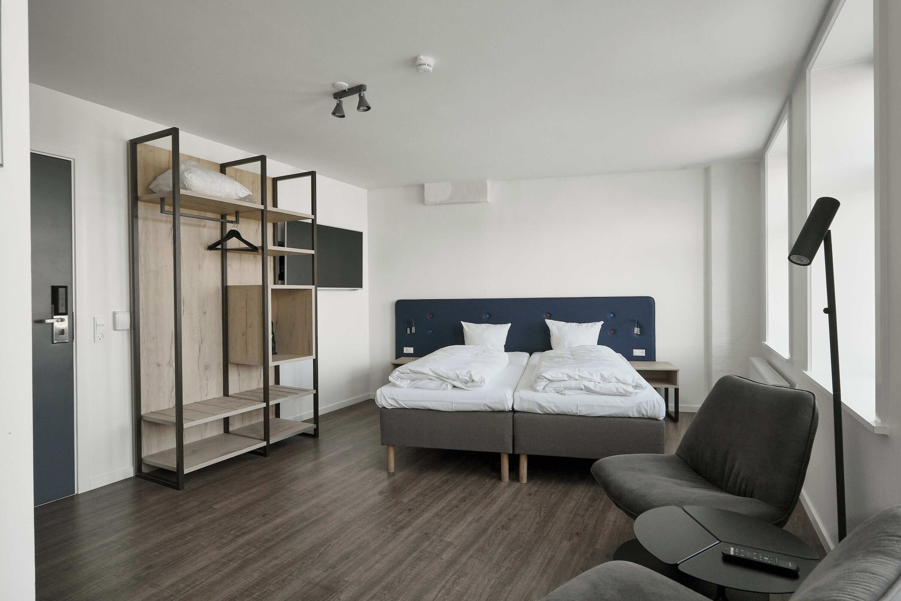 A modern hotel room with a bed, a sofa, a desk, and a wardrobe.