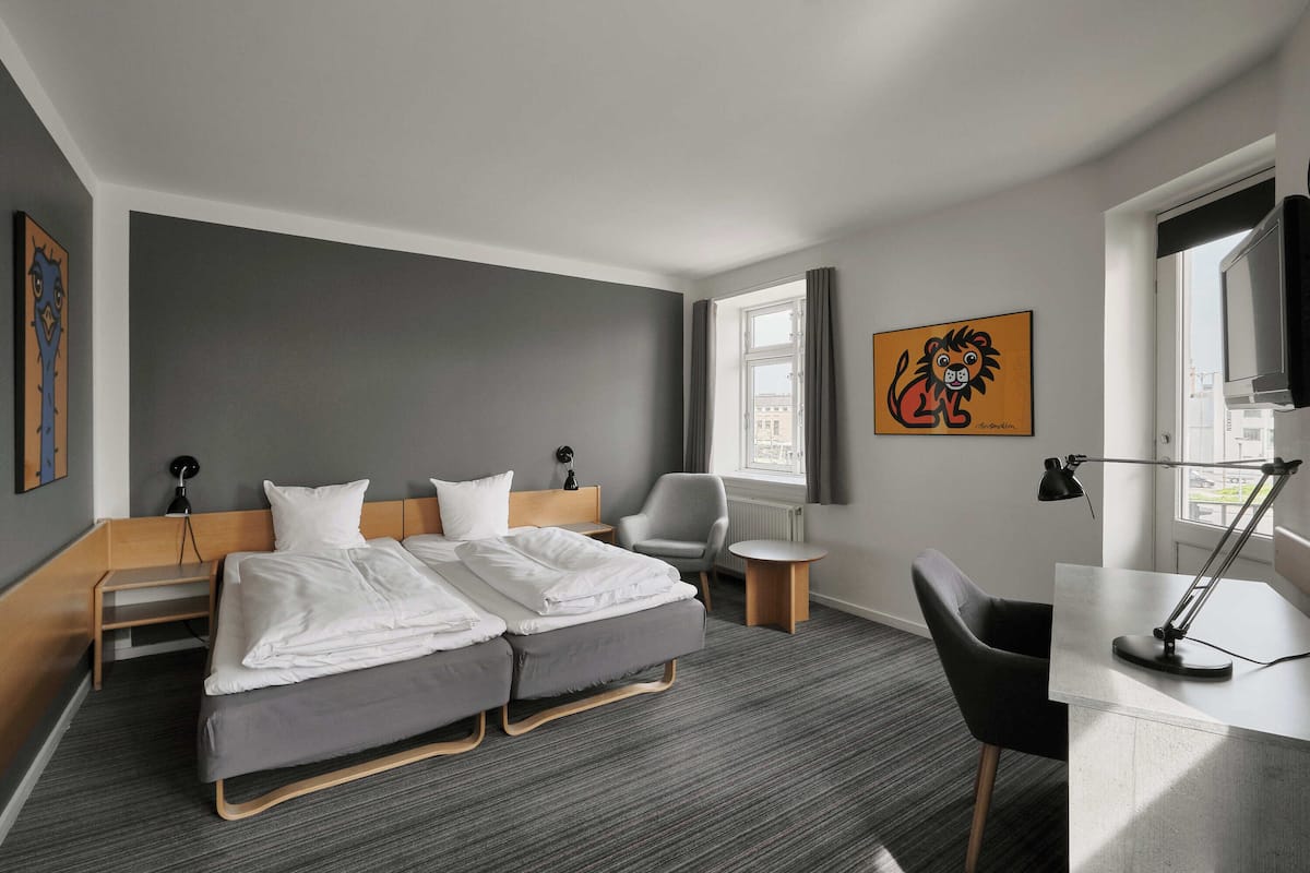 Ein modernes Hotelzimmer mit Doppelbett, Schreibtisch, Stuhl und Fernseher.