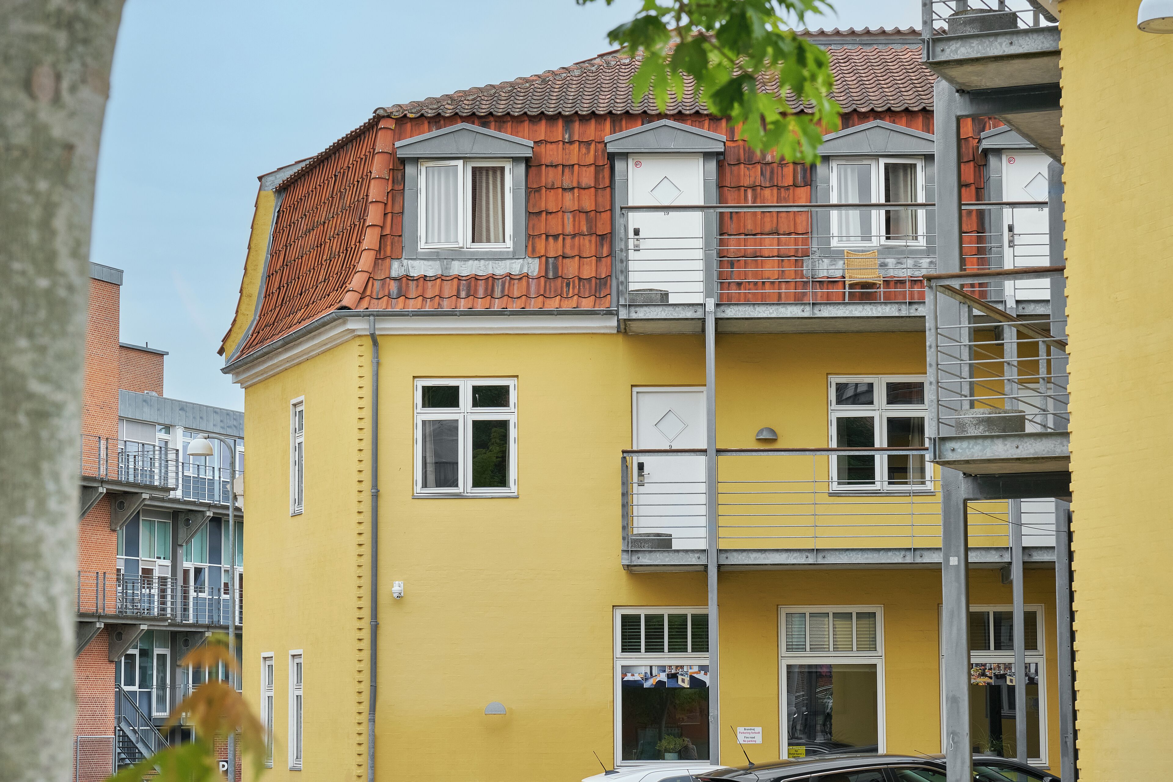 A multi-story yellow building with a red-tiled roof, multiple windows, and a visible balcony.