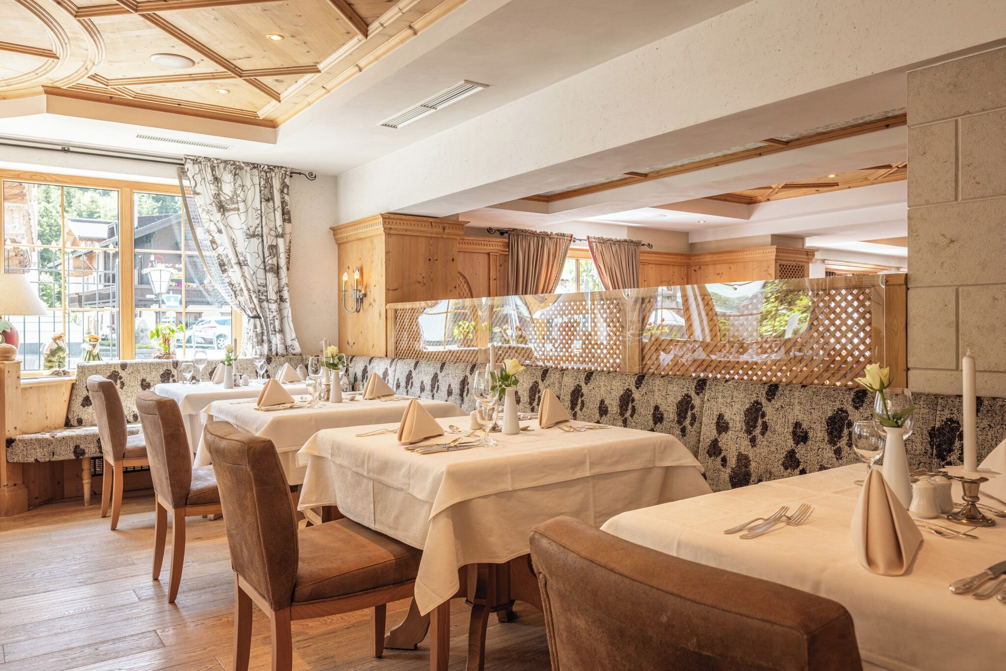 Un restaurant avec des tables et des chaises en bois, un mur décoré de motifs et une vue sur l’extérieur.