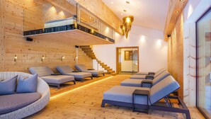 A modern spa with wooden walls, a glass-enclosed upper level, and multiple seating areas. - Hotel Gaspingerhof (Gerlos)