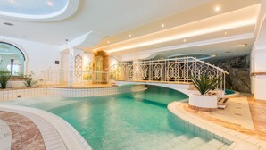 An indoor swimming pool with a white decorative bridge, tiled flooring, and a stone wall backdrop. - Hotel Gaspingerhof (Gerlos)