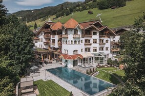 A large, multi-story building with a swimming pool, surrounded by lush greenery and hills. - Hotel Gaspingerhof (Gerlos)