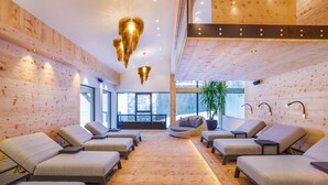 A spa room with wooden walls and ceiling, multiple massage chairs, and a large window providing a view of the outdoors. - Hotel Gaspingerhof (Gerlos)