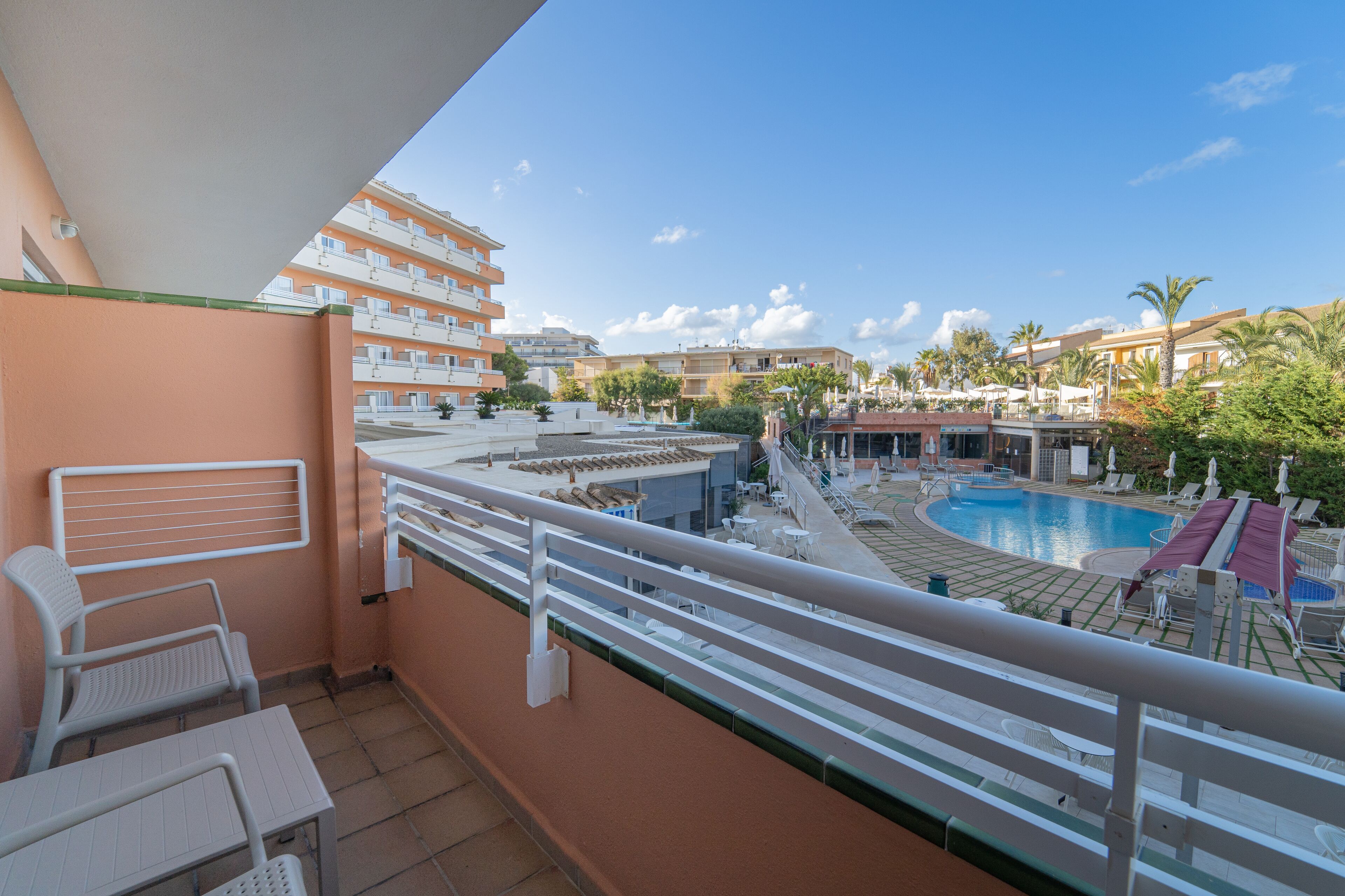 Un balcón con vista a la piscina, mobiliario exterior y cielo despejado.