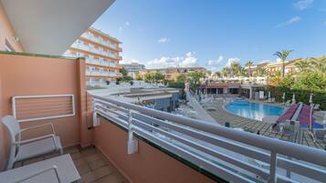 Un balcón con vista a la piscina, mobiliario exterior y cielo despejado.