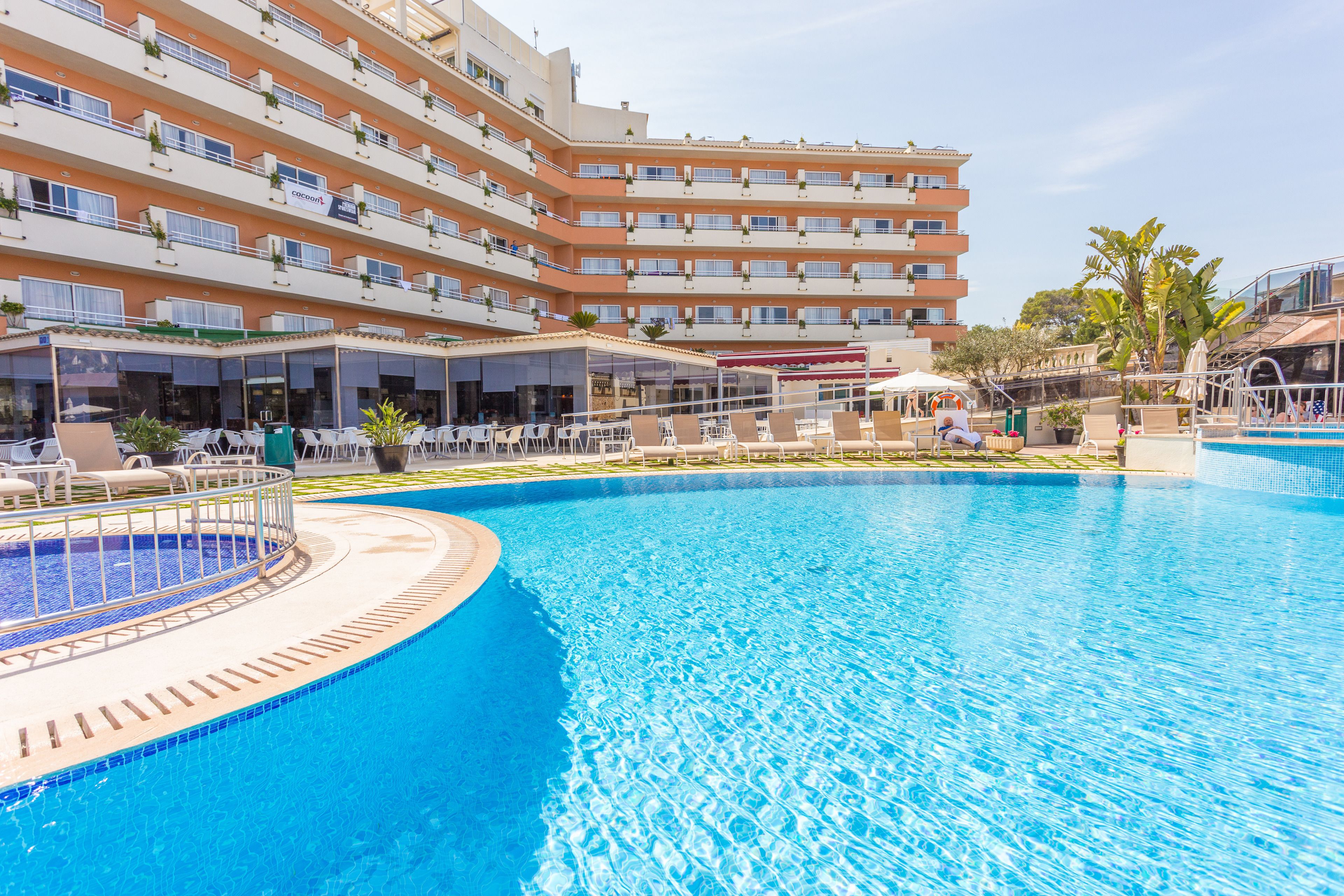 A hotel with a large pool, multiple balconies, and outdoor seating areas.