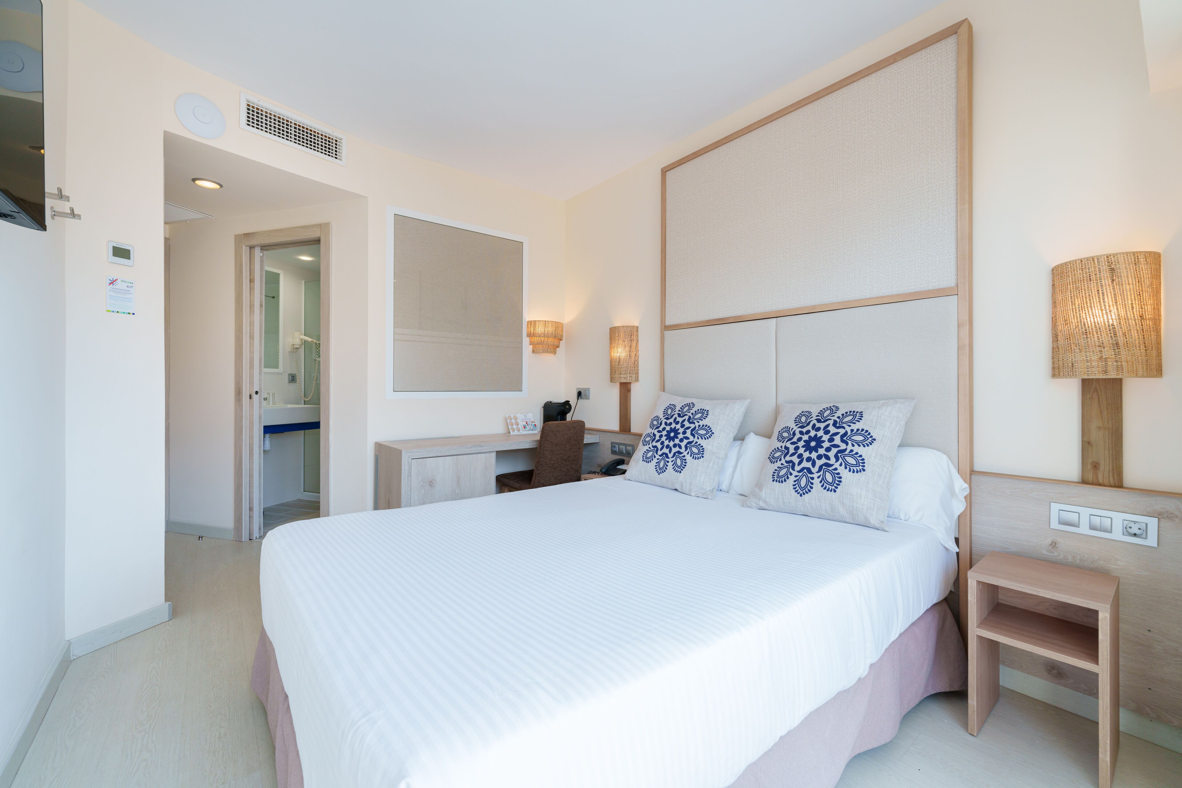 A hotel room with a large bed, a desk, a chair, and a small table.