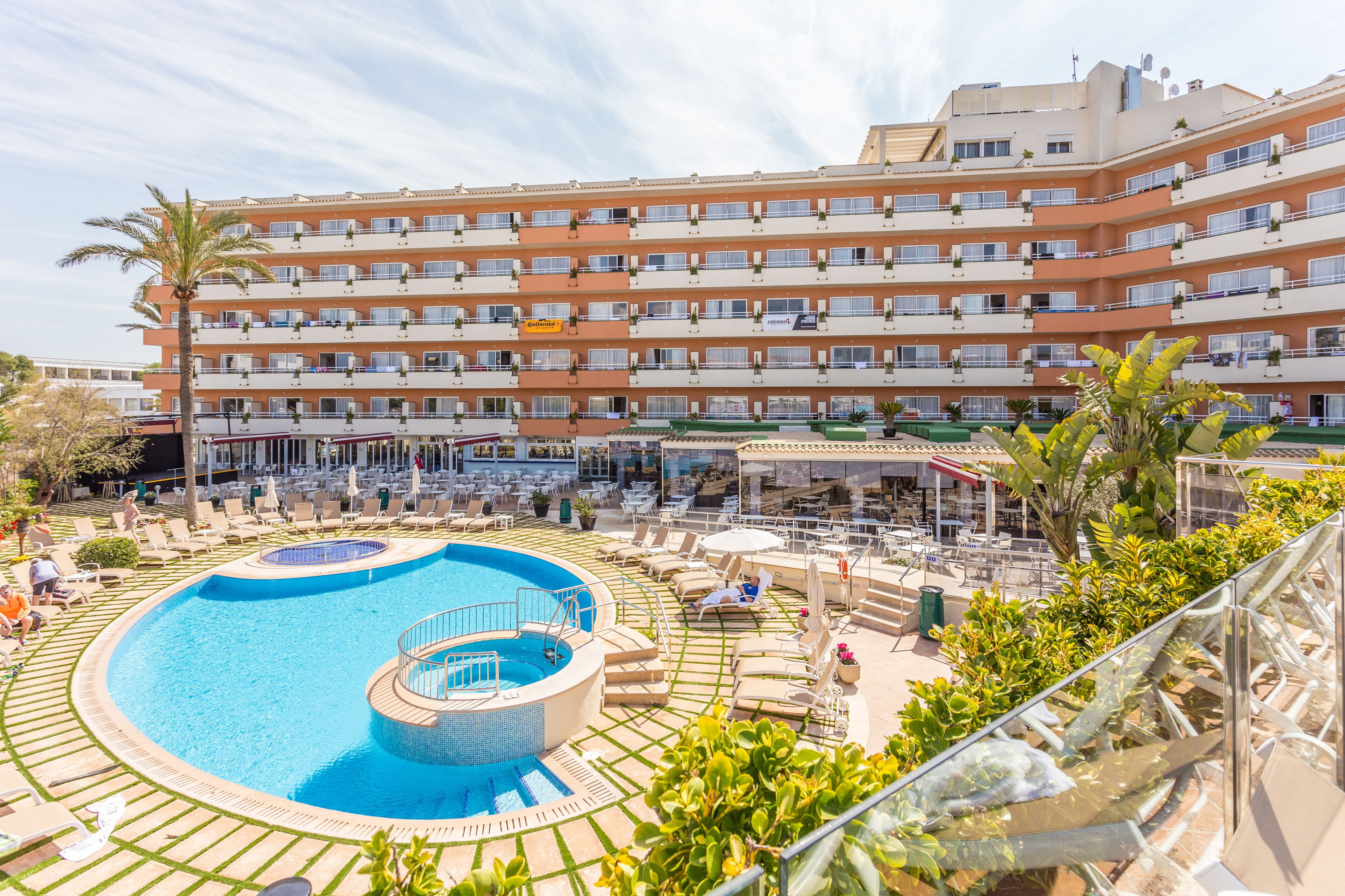 A hotel with a swimming pool, outdoor seating, and a multi-story building.