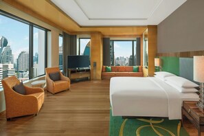 A hotel room with a large bed, two armchairs, a TV, and a city view.