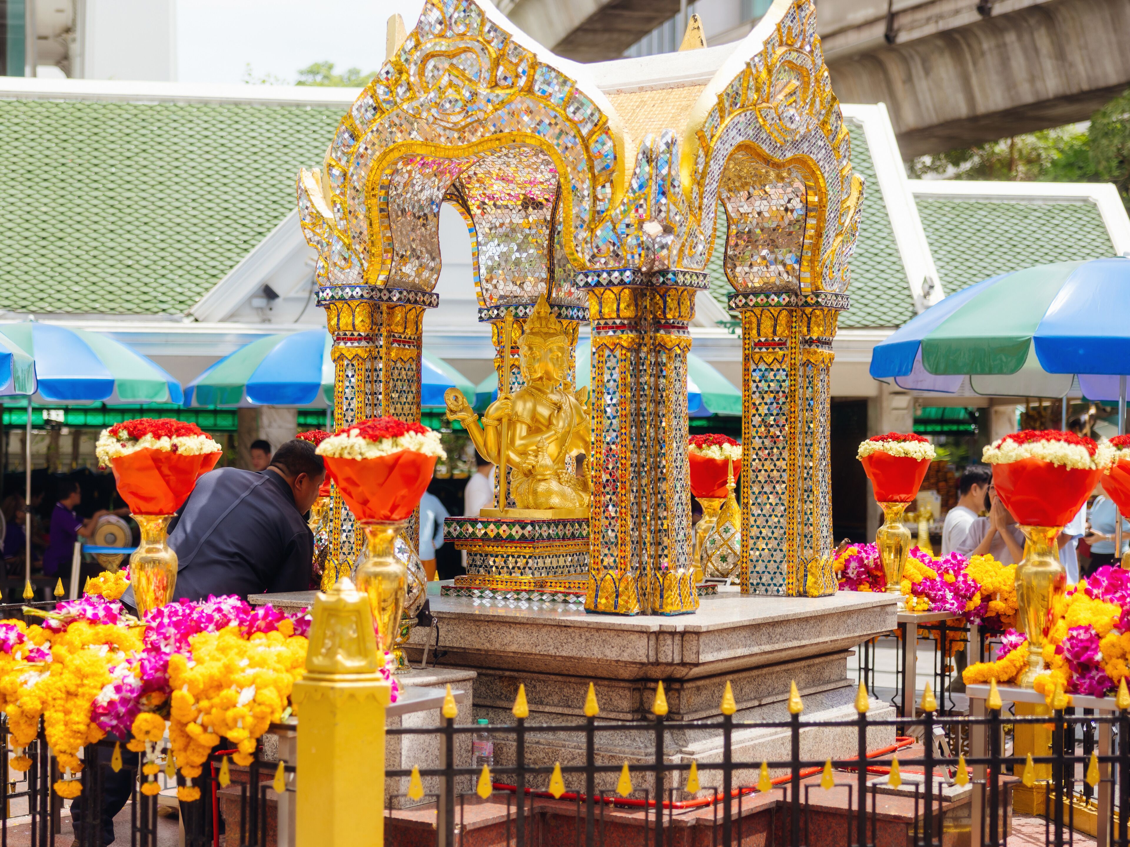 Un templo con estatuas doradas ornamentadas y pilares, rodeado de coloridas exhibiciones florales.