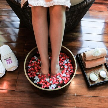 A foot bath with water, flowers, and bath salts on a wooden floor.