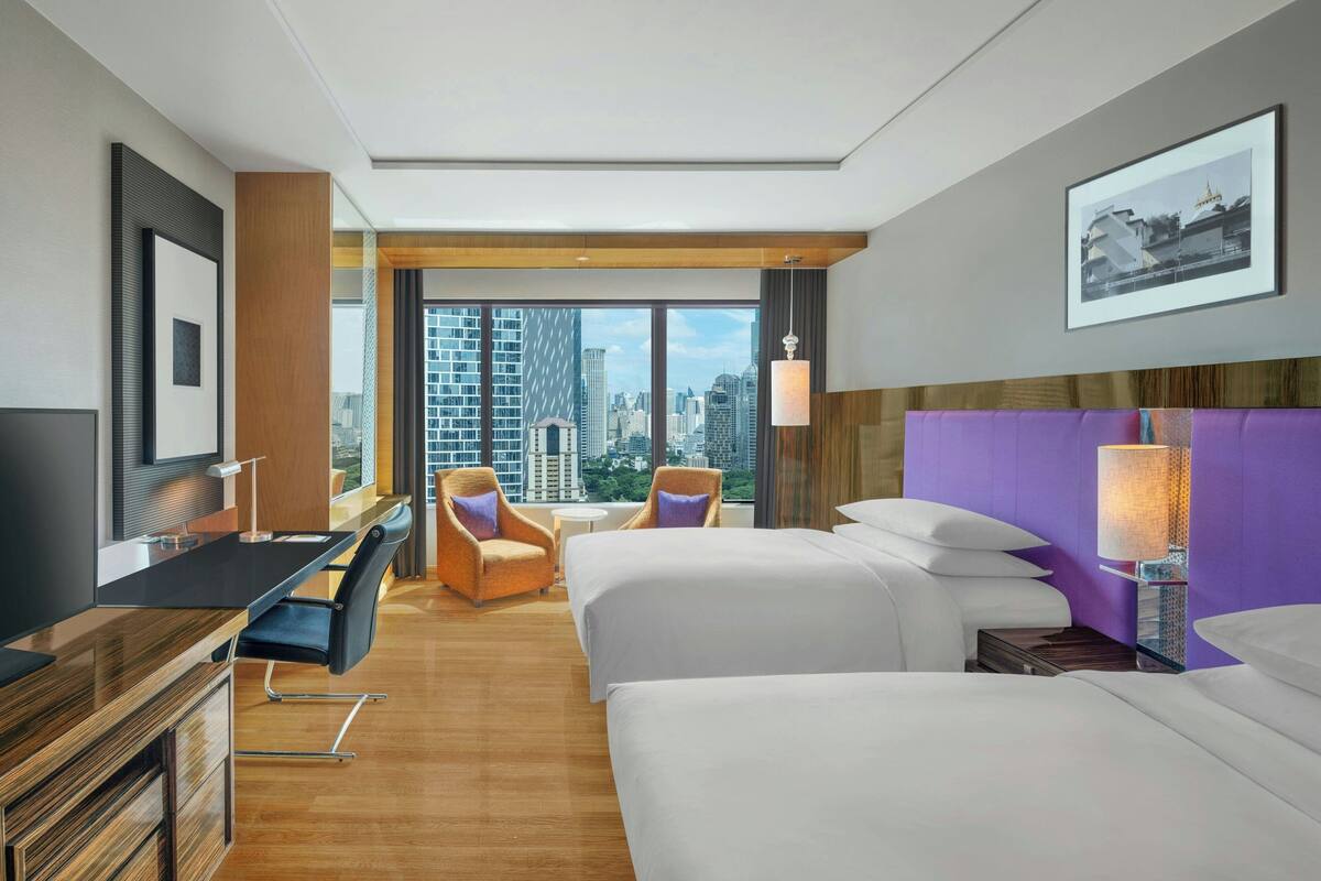 A hotel room with a city view, two beds, a desk, and a chair.