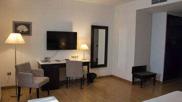 Habitación de hotel con escritorio, dos sillas, televisor, espejo, cama y una mesita.