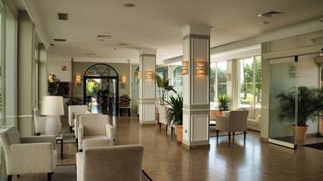 A spacious lobby with multiple seating areas, large windows, and potted plants.
