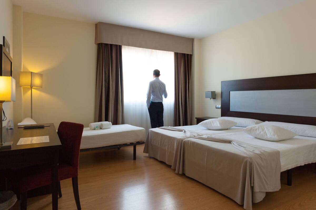 Habitación de hotel con dos camas, un escritorio, una silla y un ventanal con cortinas.