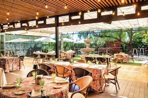 An outdoor dining area with tables set for guests, surrounded by umbrellas and a wooden pergola structure. - Hotel Las Bovedas (Badajoz)
