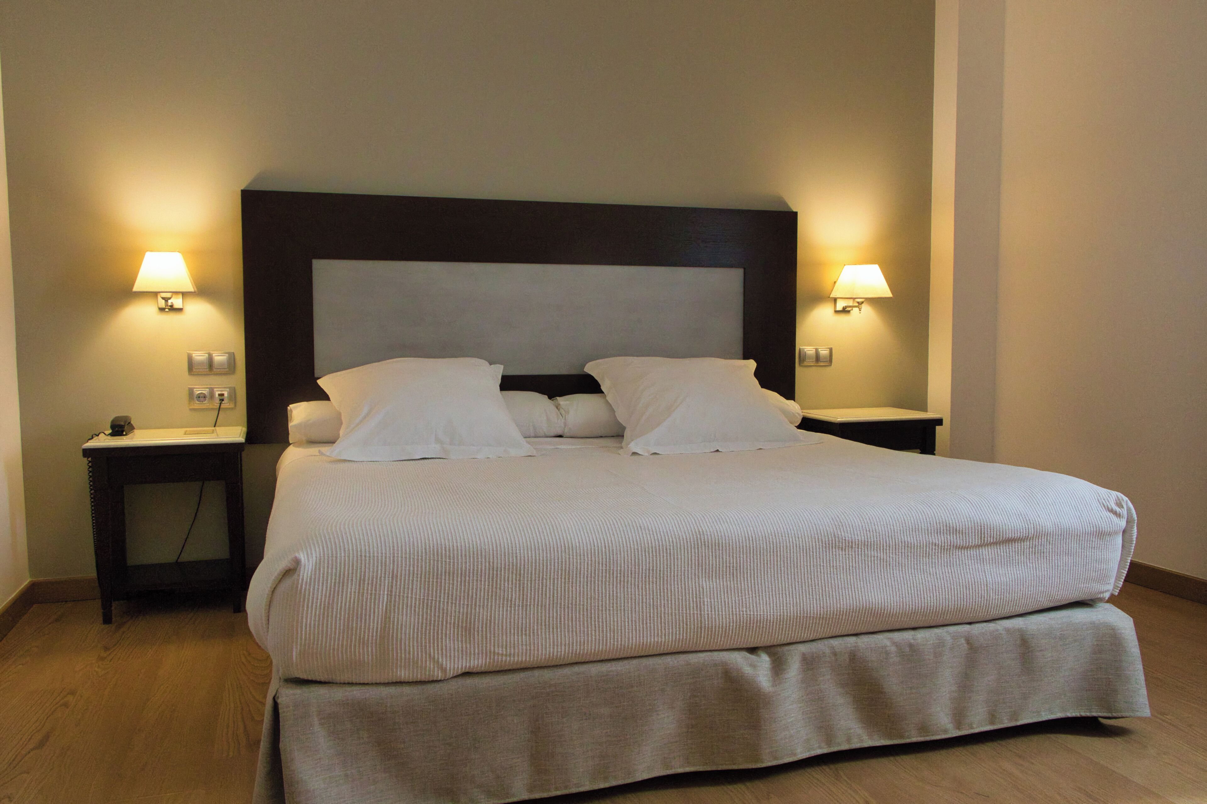 Una habitación de hotel estándar con una cama grande, dos mesitas de noche y lámparas fijadas a la pared.