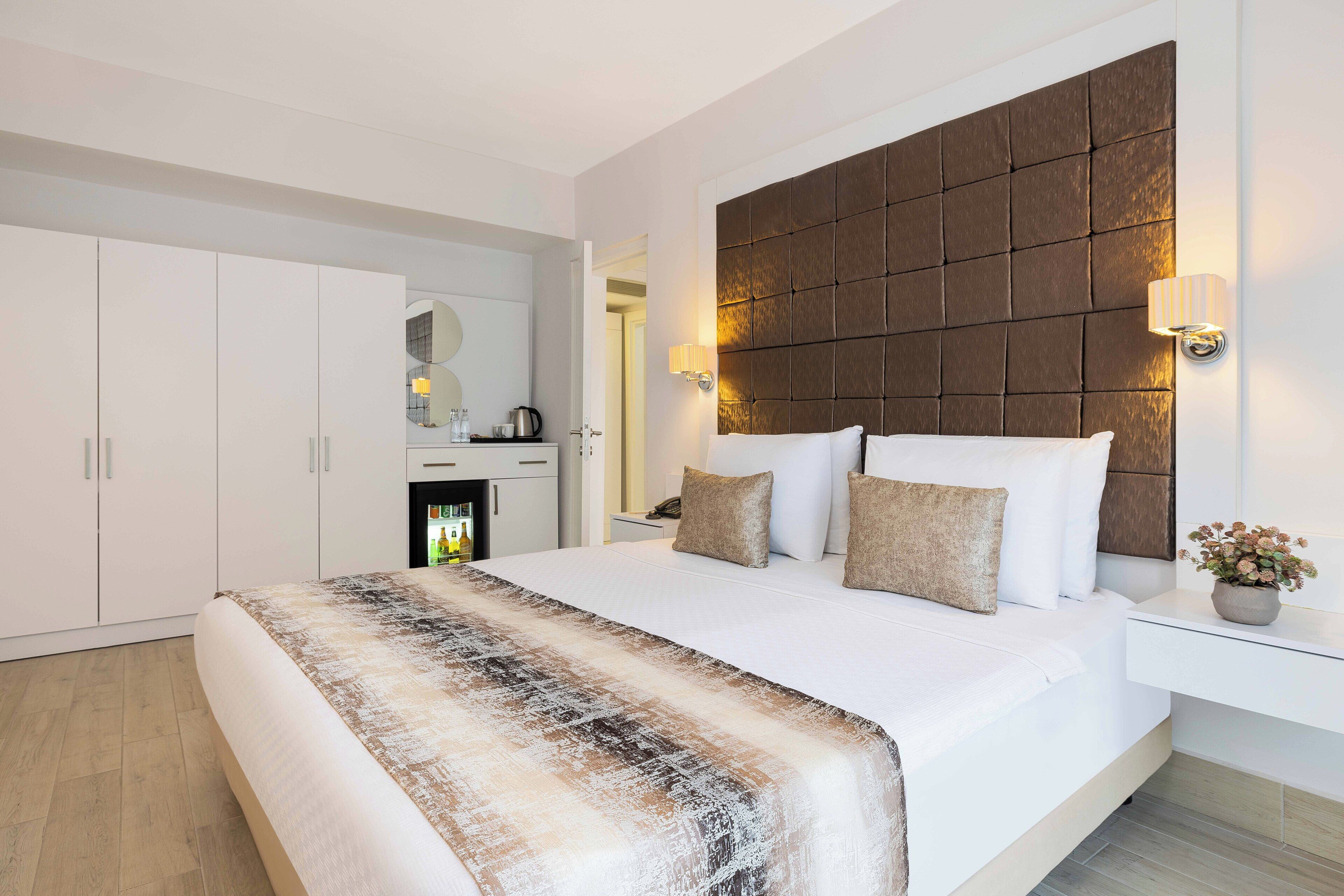 Una habitación de hotel moderna con una cama grande, un cabecero de madera, una mesita de noche con lámpara y un espejo grande en la pared.