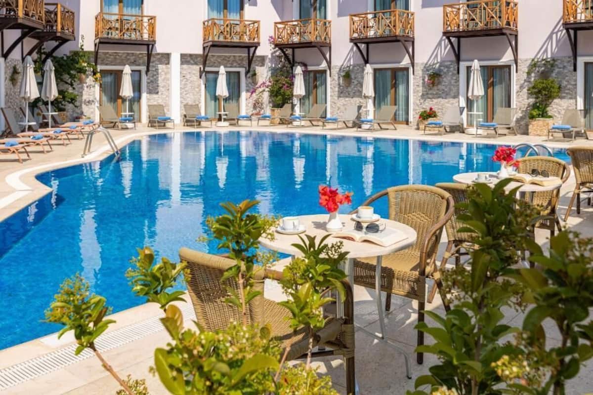 Un área junto a la piscina con sillones de descanso, una mesa con un florero y un edificio con balcones.