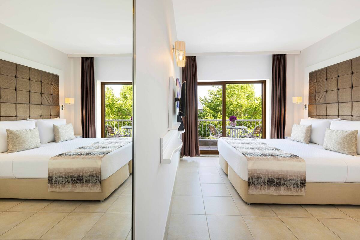 Habitación de hotel con espejo, dos camas, un ventanal grande y un balcón.