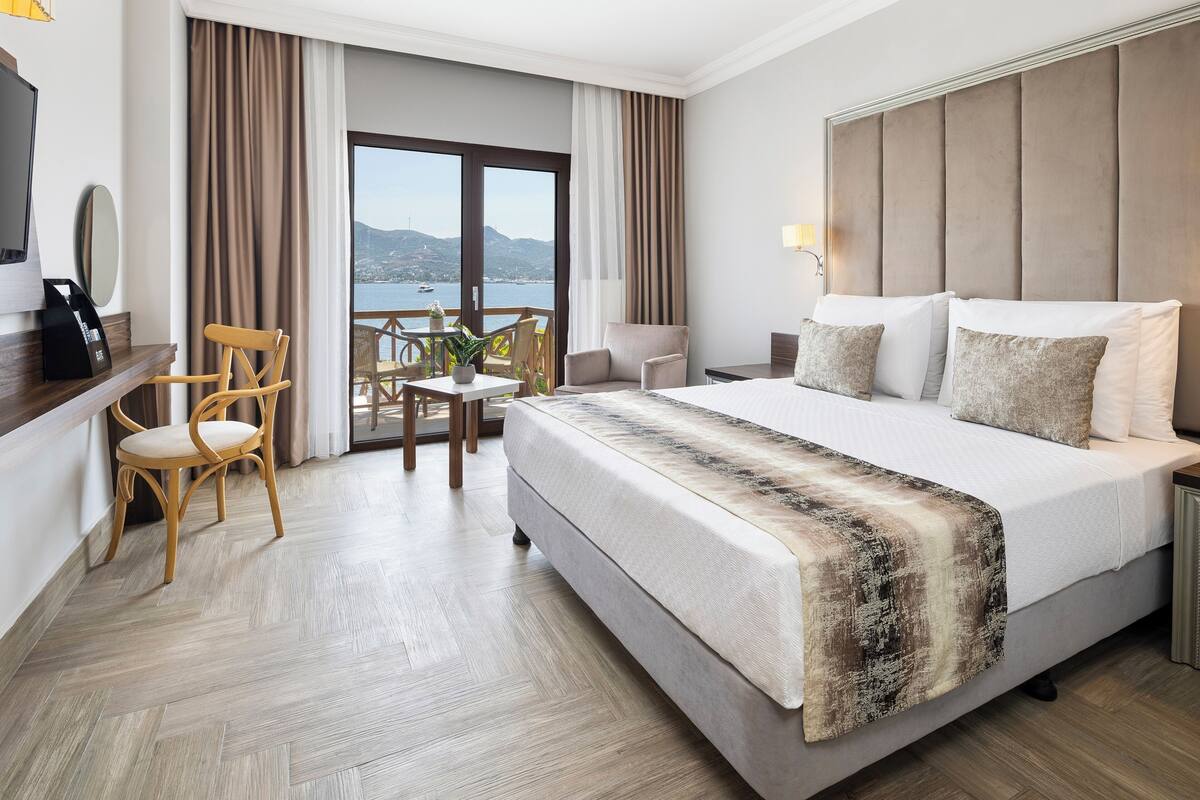 Habitación de hotel con una cama grande, un escritorio, una silla, una mesita con una planta y vista al mar.