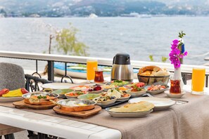 Mesa servida con diversos platos y bebidas, con vista a un cuerpo de agua.