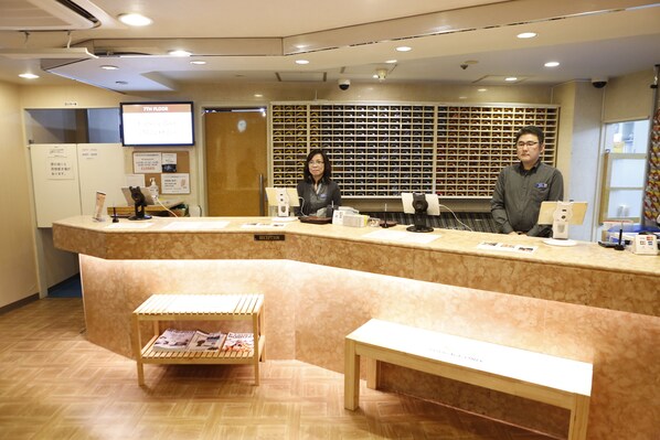 A reception desk with a computer, a telephone, and a bulletin board. There is a wooden bench and a small table with magazines.