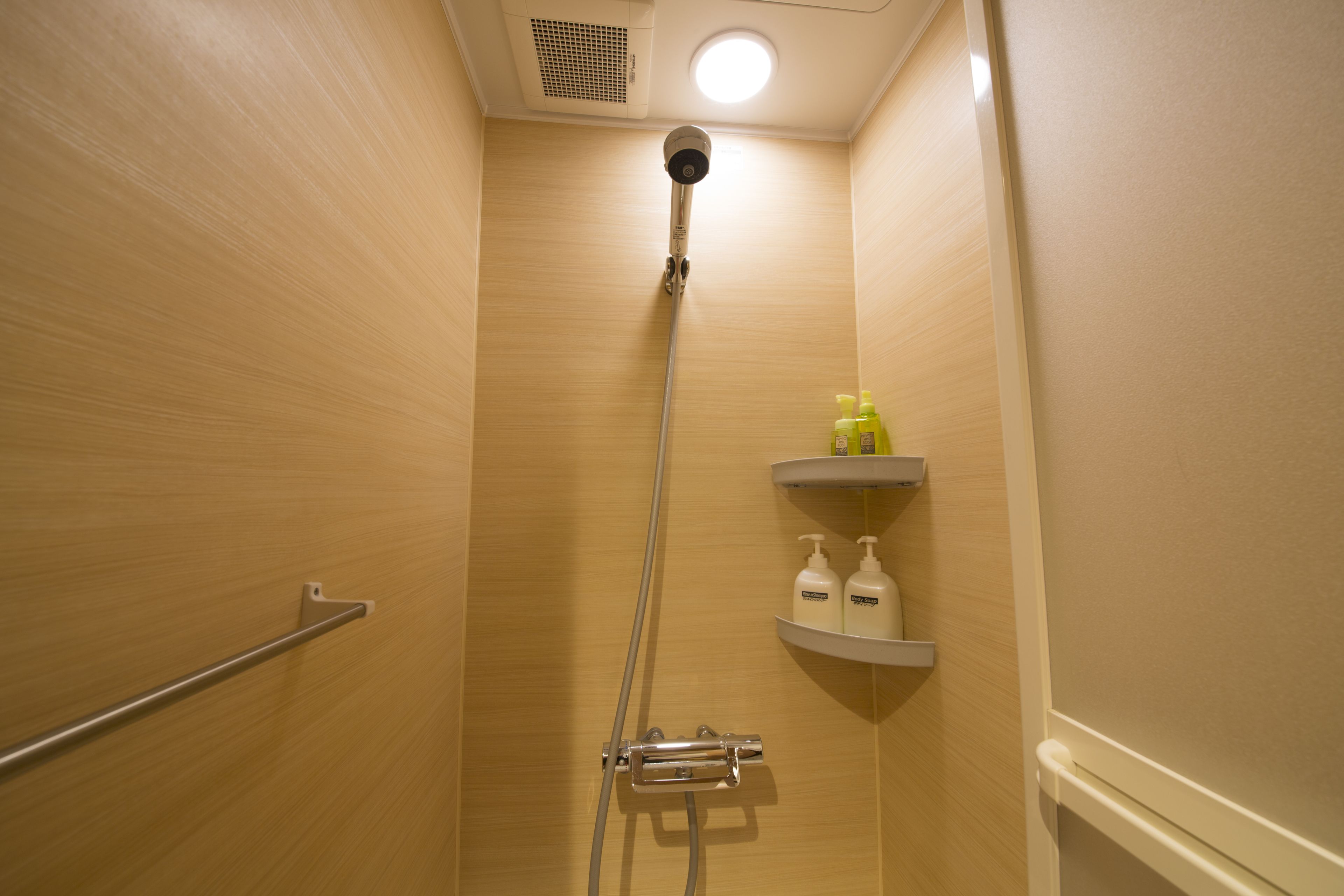 A shower with a handheld showerhead, a wall-mounted faucet, and a shelf with toiletries.