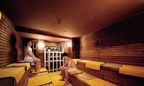 Un sauna aux murs et aux bancs en bois, avec une porte en verre donnant sur un espace douche.