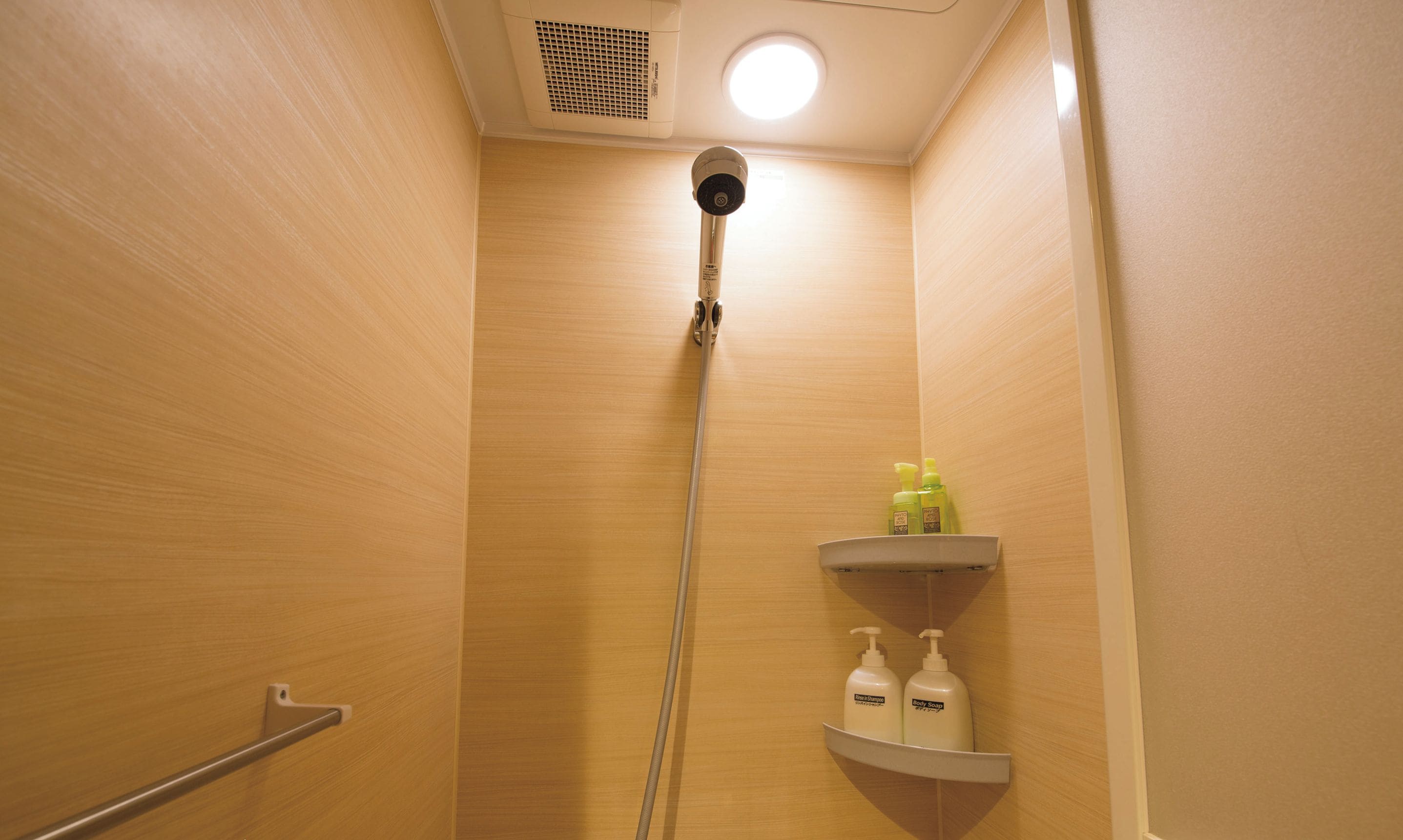 Un cabina de ducha privada con interior de madera, un cabezal de ducha en el techo y dos estantes con artículos de aseo.